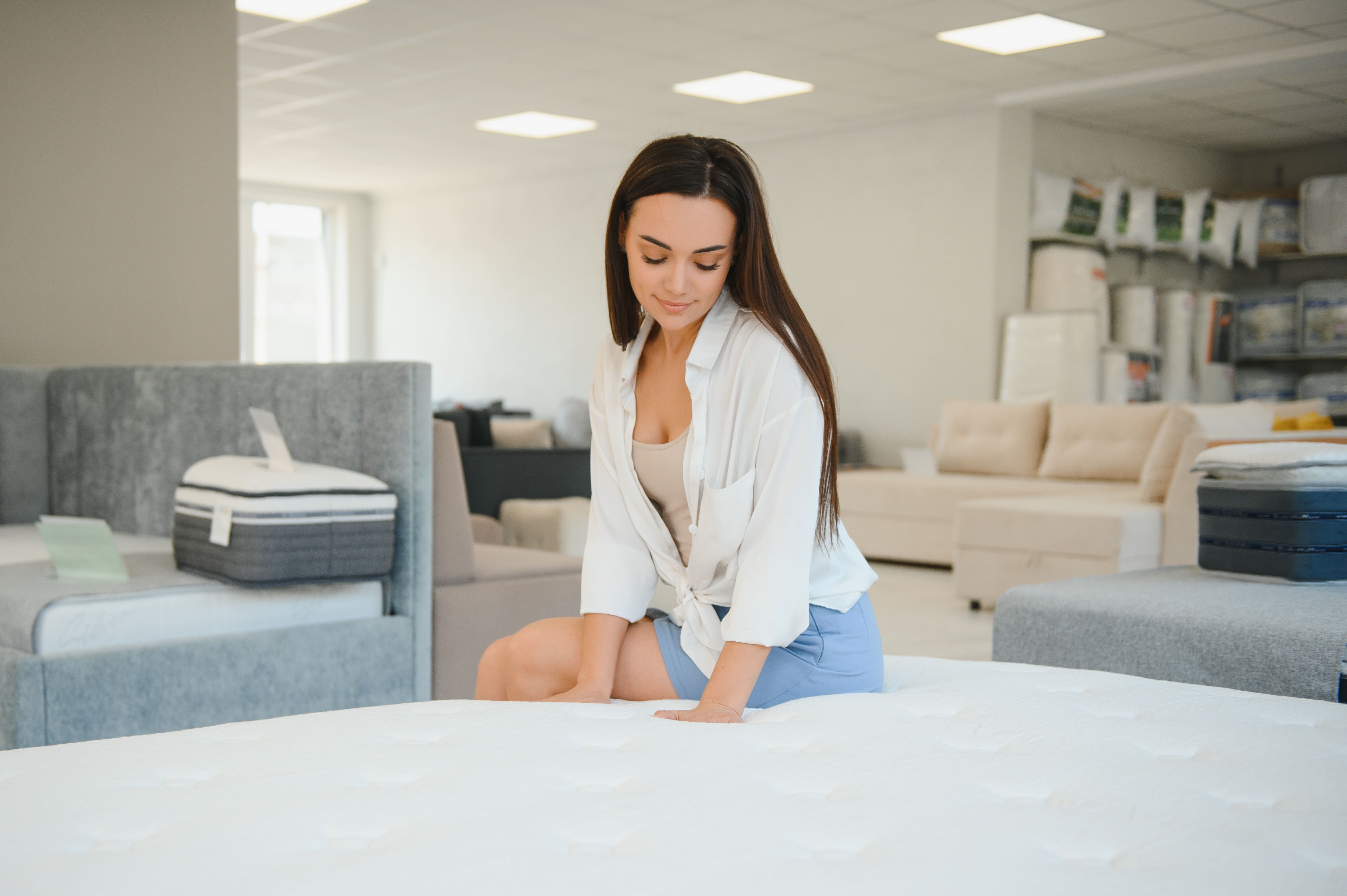 Femme assise sur un matelas posé sur un sommier à lattes dans une chambre lumineuse